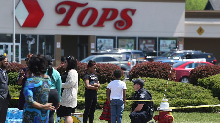 A Buffalo police officer talks to children at the scene of Saturday's shooting as Tops is seen in the background