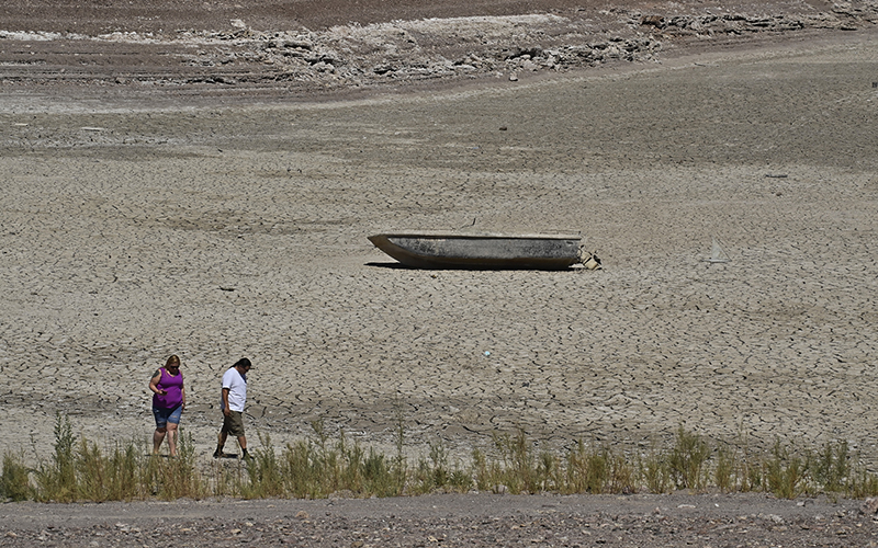 A formerly sunken boat sits on cracked earth as two people walk past in the foreground