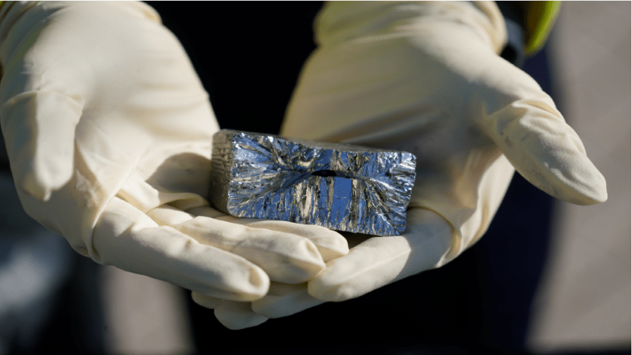 Hands in rubber gloves hold a silver block of mineral.