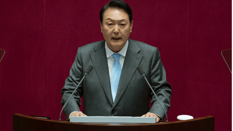 South Korean President Yoon Suk yeol stands at a podium in front of a red background.