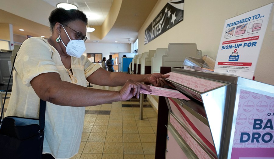 A woman wearing a mask drops off a ballot.