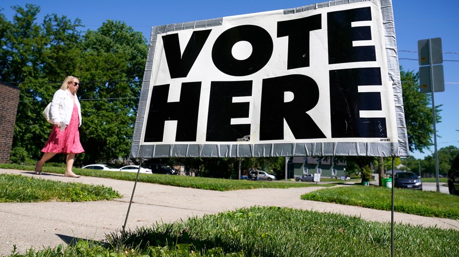 A woman walks near a "vote here" sign.