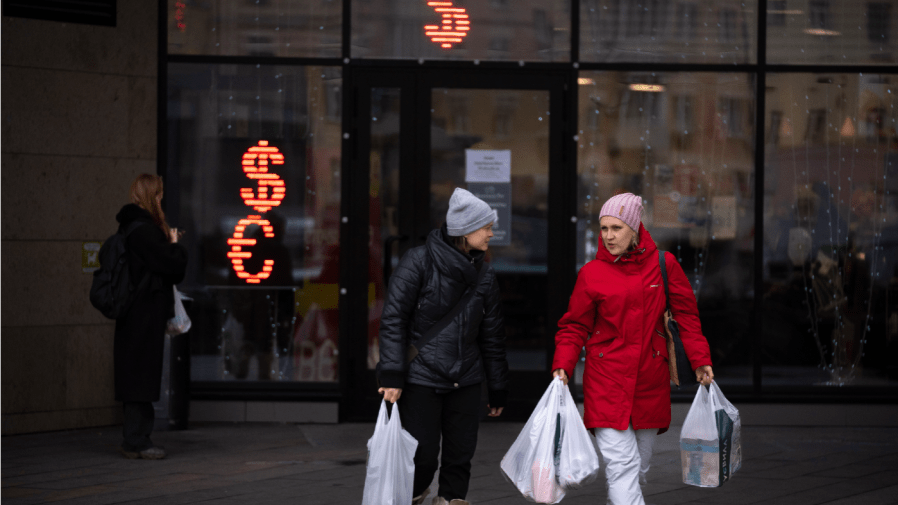 Two women walk past a currency exchange office screen displaying the exchange rates of U.S. Dollar and Euro to Russian Rubles in Moscow, Russia, Friday, April 1, 2022.