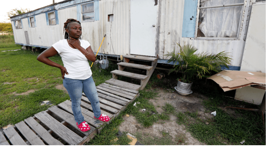 A woman in a white t-shirt stands on the steps leading to her trailer.