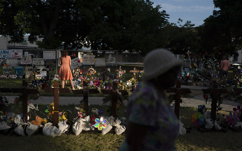 People visit a memorial made up of crosses and a decorated fence in Uvalde, Texas