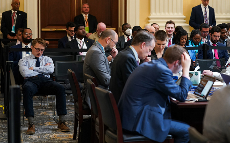 Members of the public and press are seen sitting at desks and in chairs