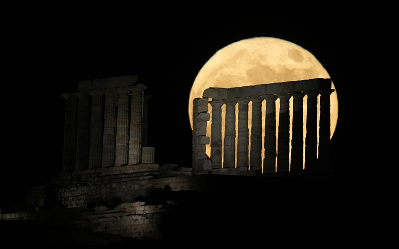 The strawberry supermoon rises behind the ancient temple of Poseidon