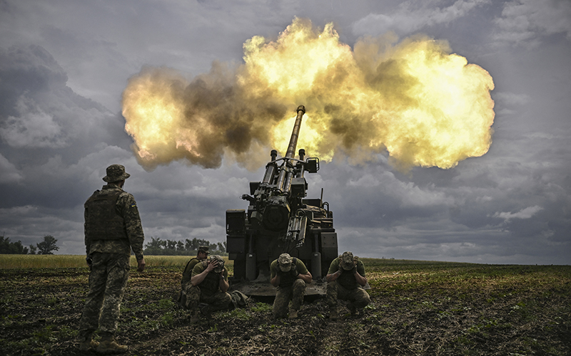 Ukrainian servicemen take cover as they fire with a French self-propelled 155 mm/52-caliber gun, creating a cloud of smoke under a dark sky