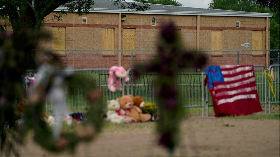 Windows at Robb Elementary School are boarded are seen behind a memorial