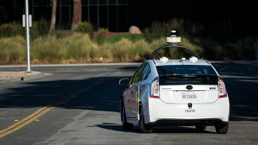 A white Nuro autonomous self-driving vehicle drives alone on a road