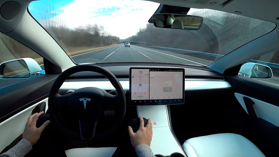 The interior of a white Tesla Model 3 is seen as the car drives down a road on autopilot.