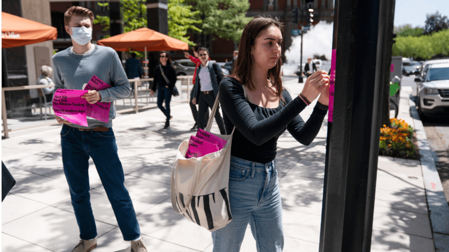 George Washington University student Kai Nilsen, left, watches as American University student Magnolia Mead as they put up posters near the White House promoting student loan debt forgiveness, Friday, April 29, 2022, in Washington.