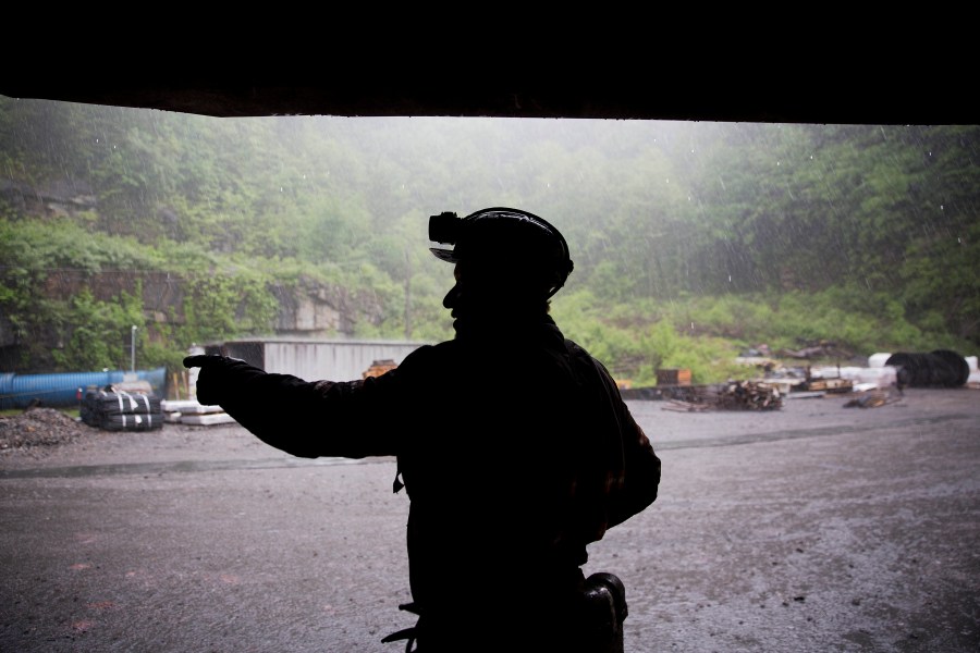 A coal miner points to distance while sheltering from the rain.