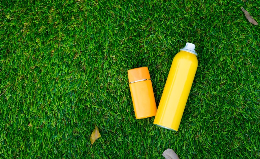 top down view of stick and spray sunscreen on grass