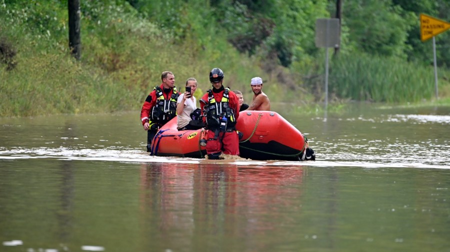 Members of the Winchester, Ky., Fire Department walk inflatable boats across flood waters over a road in Jackson, Ky., to pick up people stranded by the floodwaters on Thursday, July 28, 2022.