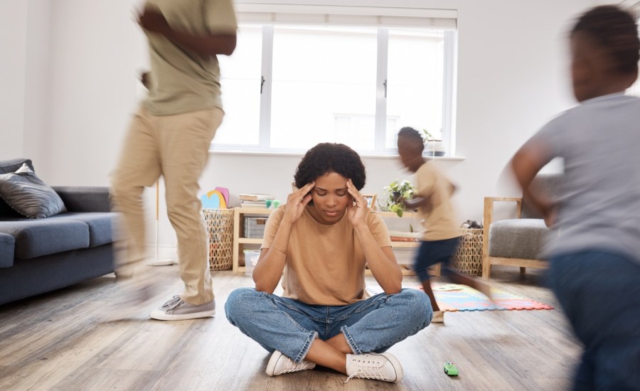 stock image of woman sitting on living room floor with children and man running around