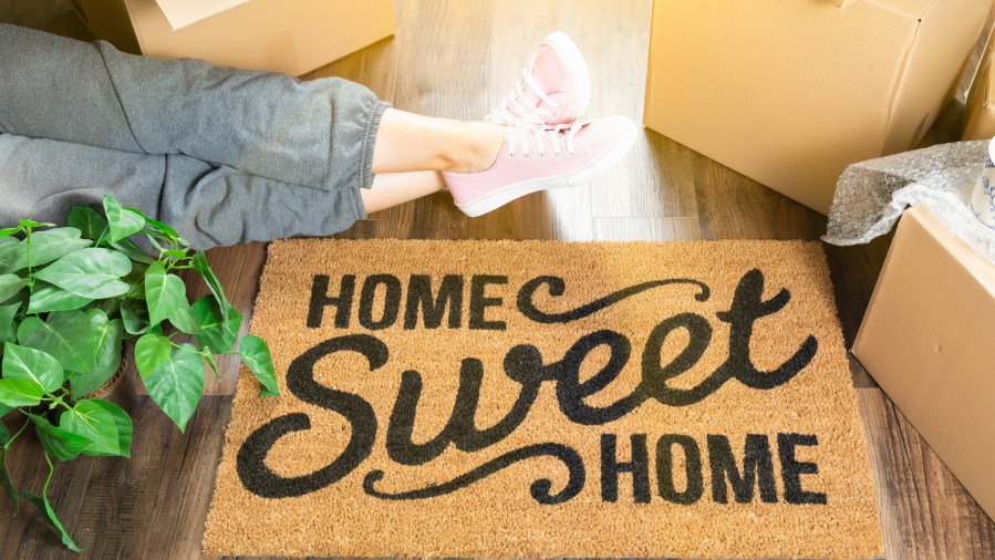 Woman Wearing Sweats Relaxing Near Home Sweet Home Welcome Mat, Moving Boxes and Plant.