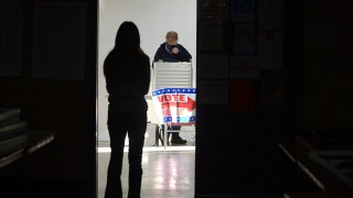 First-time voter Baylee Fidler, 19, waits in the doorway for a voting booth as a man completes his vote at the voting booth