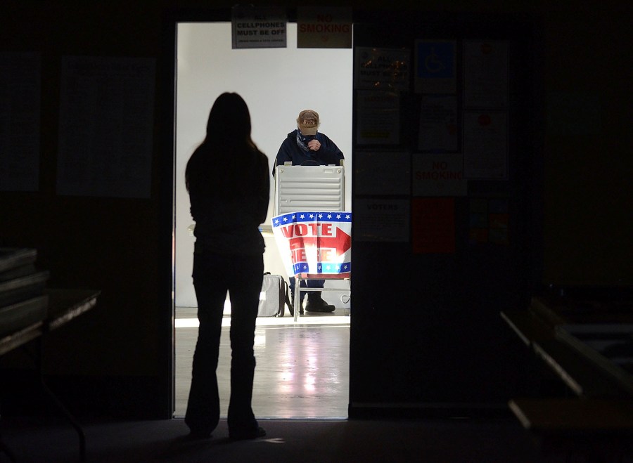 First-time voter Baylee Fidler, 19, waits in the doorway for a voting booth as a man completes his vote at the voting booth