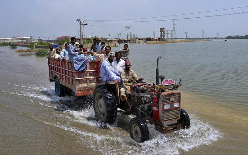 People travel in a trailer pulled by a tractor through a flooded area in Pakistan
