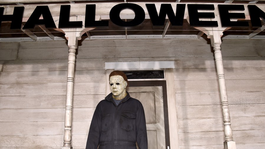 Michael Myers in white mask standing in front of creepy house with the title "HALLOWEEN" at the top