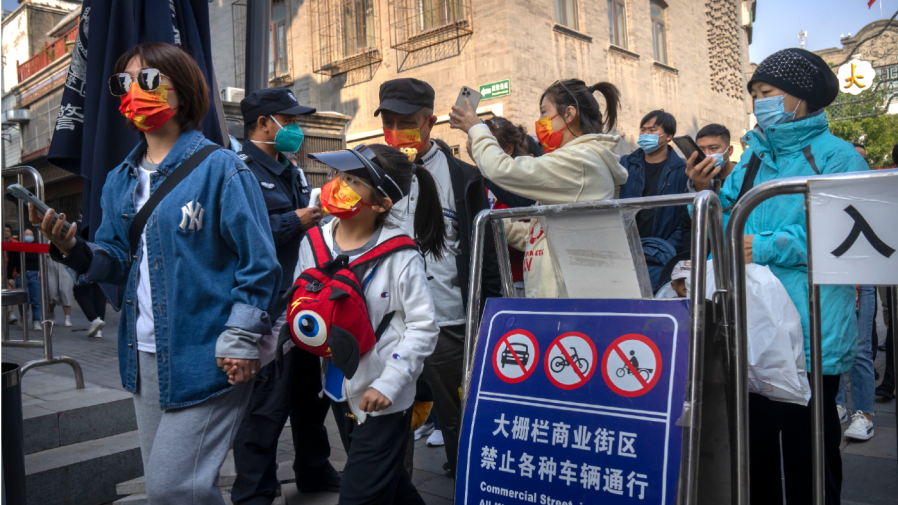 People wearing face masks show their results on a health checking app to a security guard as they enter a tourist shopping street in Beijing, Friday, Oct. 7, 2022.