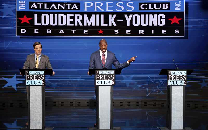 Sen. Raphael Warnock, center, gestures next to an empty Atlanta Press Club podium set up for Republican challenger Herschel Walker