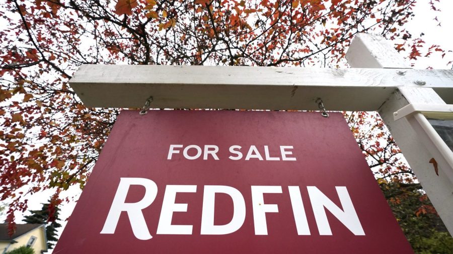 A close-up of a Redfin "for sale" sign is seen in front of trees.