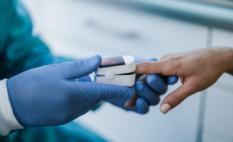 health care worker with gloves on puts a pulse oximeter on the finger of a person with darker skin