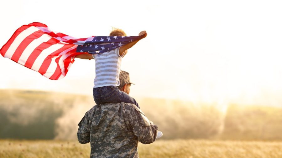 Man in army with child on shoulder holding U.S. flag.