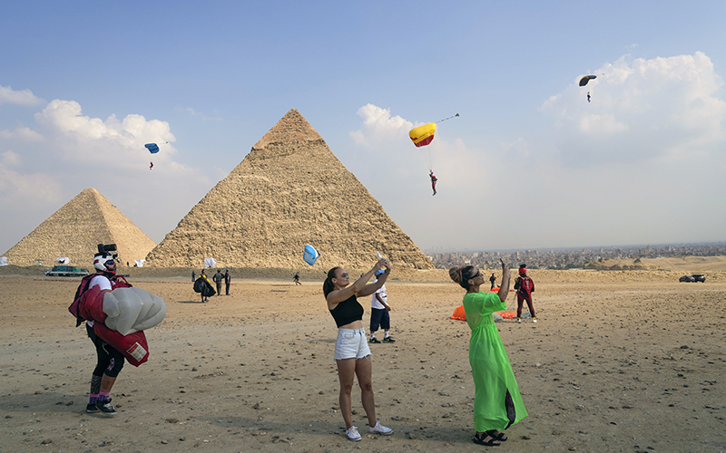 Tourists film parachutists as they approach the Giza Pyramids