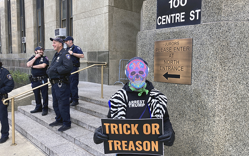 A protester wearing an "Arrest Trump" shirt holds a sign that reads "Trick or Treason"