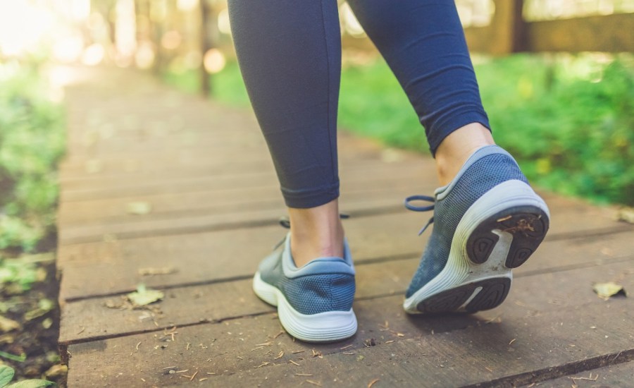 person's feet in sneakers on a boardwalk outdoors, view from behind