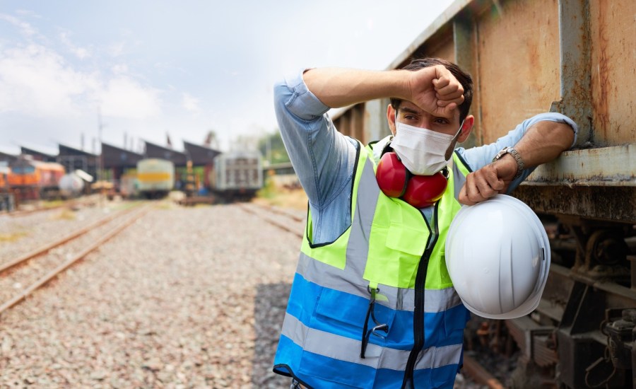 construction worker standing outside next to a structure, with back of hand to forehead