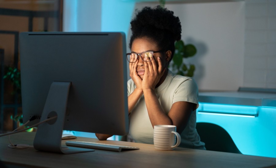 young Black woman sitting at a desk in front of computer monitor, massaging her eyes