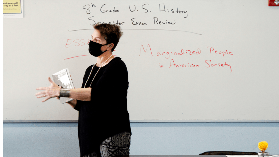 History teacher Wendy Leighton holds a copy of "They Called us Enemy," about the internment of Japanese Americans, while speaking about marginalized with her students at Monte del Sol Charter School