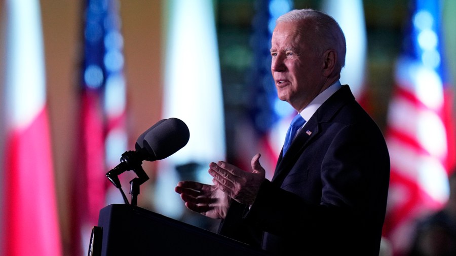 Joe Biden gestures at a podium as he speaks in front of flags which are blurred in the background.