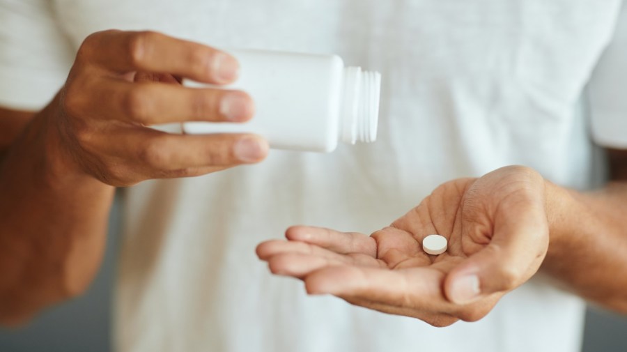 man with pill bottle in one hand and a pill in the palm of the other hand