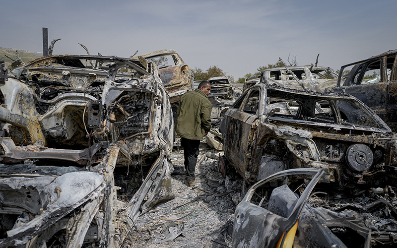 A Palestinian man walks between scorched cars in a scrapyard