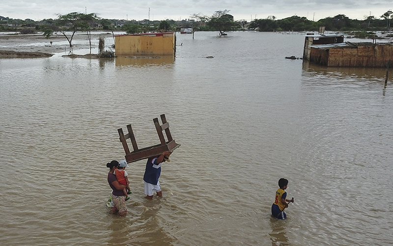A man carries a table through a Chiclayo, Peru, street flooded by heavy rains
