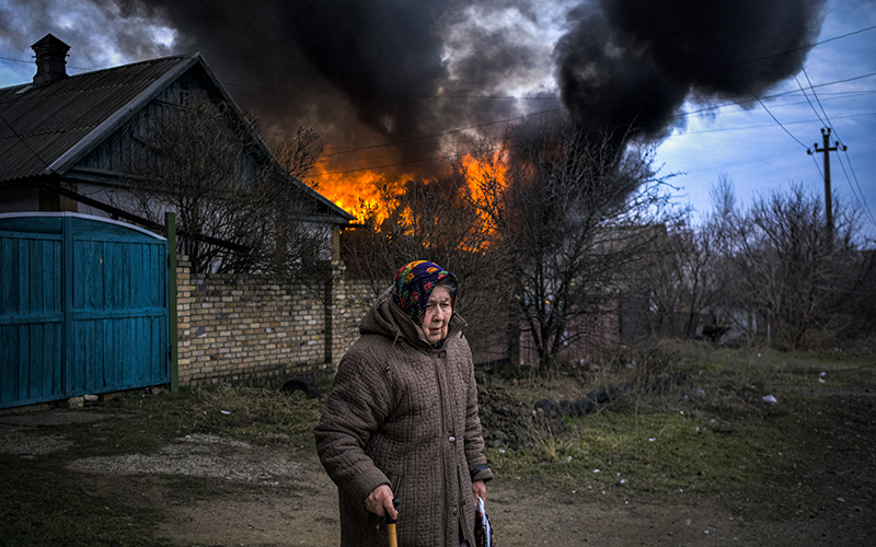 An elderly woman stands near a burning building following shelling in Kostyantynivka, Donetsk region