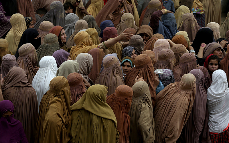 Women gather and wait to get a free sack of wheat flour at a distribution point, in Peshawar, Pakistan