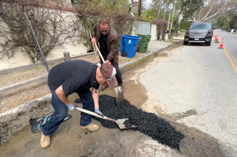 This video still image provided by The Office of Arnold Schwarzenegger, shows former California Governor Arnold Schwarzenegger, center back, repairing a pot hole on a street in his Los Angeles neighborhood on Tuesday, April 11, 2023. Fed up by an enormous pothole in his neighborhood, Schwarzenegger picked up a shovel and filled it himself. (The Office of Arnold Schwarzenegger via AP)