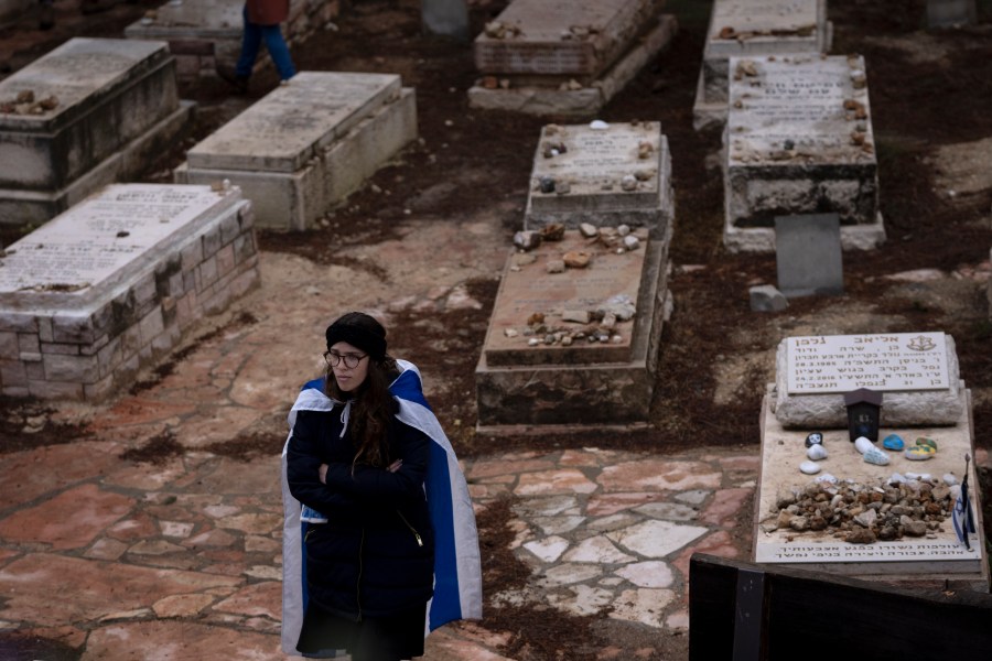 A mourner draped in the Israeli flag attends the funeral for Lucy Dee at a cemetery in the West Bank Jewish settlement of Kfar Etzion, Tuesday, April 11, 2023. The British-Israeli woman died of wounds from an April 7 shooting attack that killed her daughters, Maia and Rina Dee, by Palestinian gunmen in the West Bank. (AP Photo/Maya Alleruzzo)