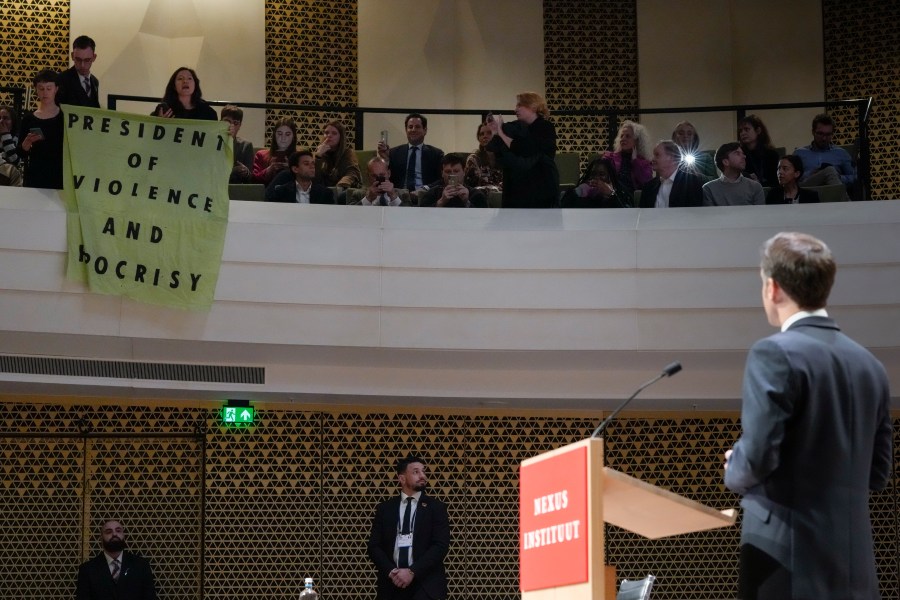 French President Emmanuel Macron looks at demonstrators unfolding a banner reading "President of Violence and Hypocrisy" as he explains his vision on the future of Europe during a lecture in a theatre in The Hague, Netherlands, Tuesday, April 11, 2023. (AP Photo/Peter Dejong)