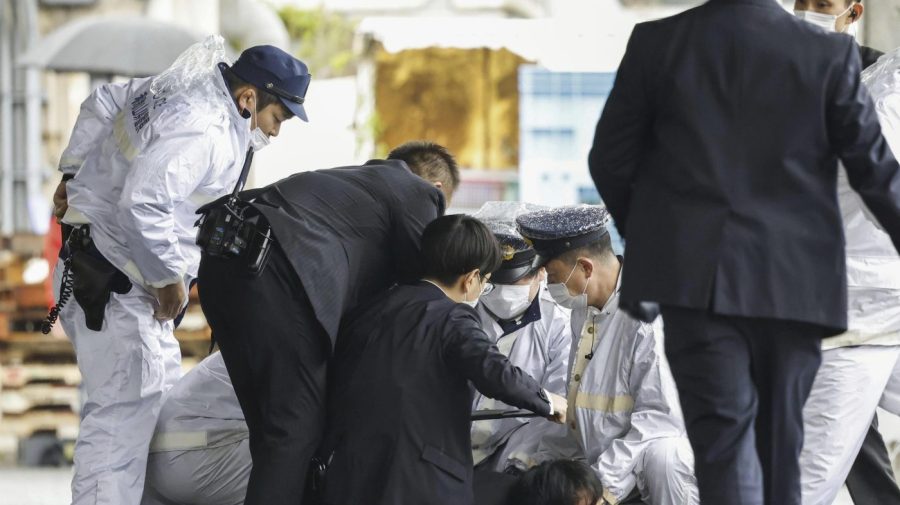 A man believed to be a suspect, center on the ground, is caught by police after he allegedly threw “the suspicious object,” as Japanese Prime Minister Fumio Kishida visited Saikazaki port for an election campaign event in Wakayama, western Japan Saturday, April 15, 2023. Kishida was evacuated unharmed Saturday after someone threw an explosive device in his direction while he was campaigning at the fishing port in western Japan, officials said.(Kyodo News via AP)