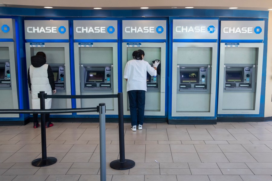 FILE - A worker, right, cleans an ATM as a customer uses another at a Chase branch in the Queens borough of New York on March 24, 2020. Banks are paying up for savers' deposits in a much bigger way than they have in more than a decade, based on the earnings reports from the nation's biggest banks out over the past week. (AP Photo/Mary Altaffer, File)