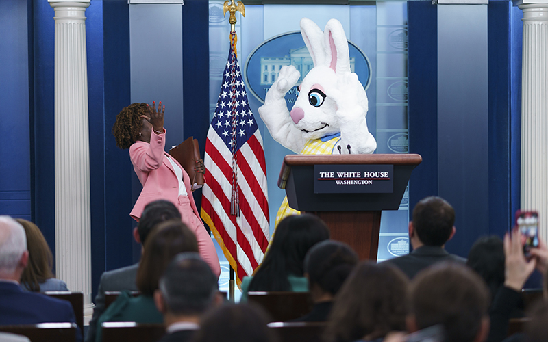 White House press secretary Karine Jean-Pierre raises her arms in surprise at the Easter Bunny, who is standing behind a podium, before a news conference