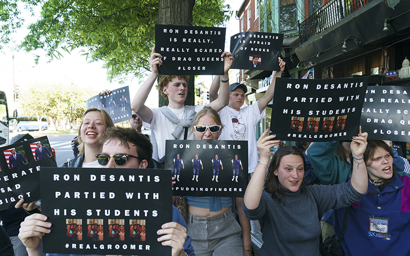 Gay rights protesters against Florida Gov. Ron DeSantis (R) hold signs that read "Ron DeSantis partied with his students"