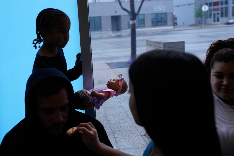 Charlotte, a Venezuelan immigrant, stands in silhouette holding a baby doll as her family and others take shelter in the Chicago Police Department's 16th District station on Monday, May 1, 2023. Chicago has seen the number of new arrivals grow tenfold in recent days. Shelter space is scarce and migrants awaiting a bed are sleeping on floors in police stations and airports. (AP Photo/Charles Rex Arbogast)